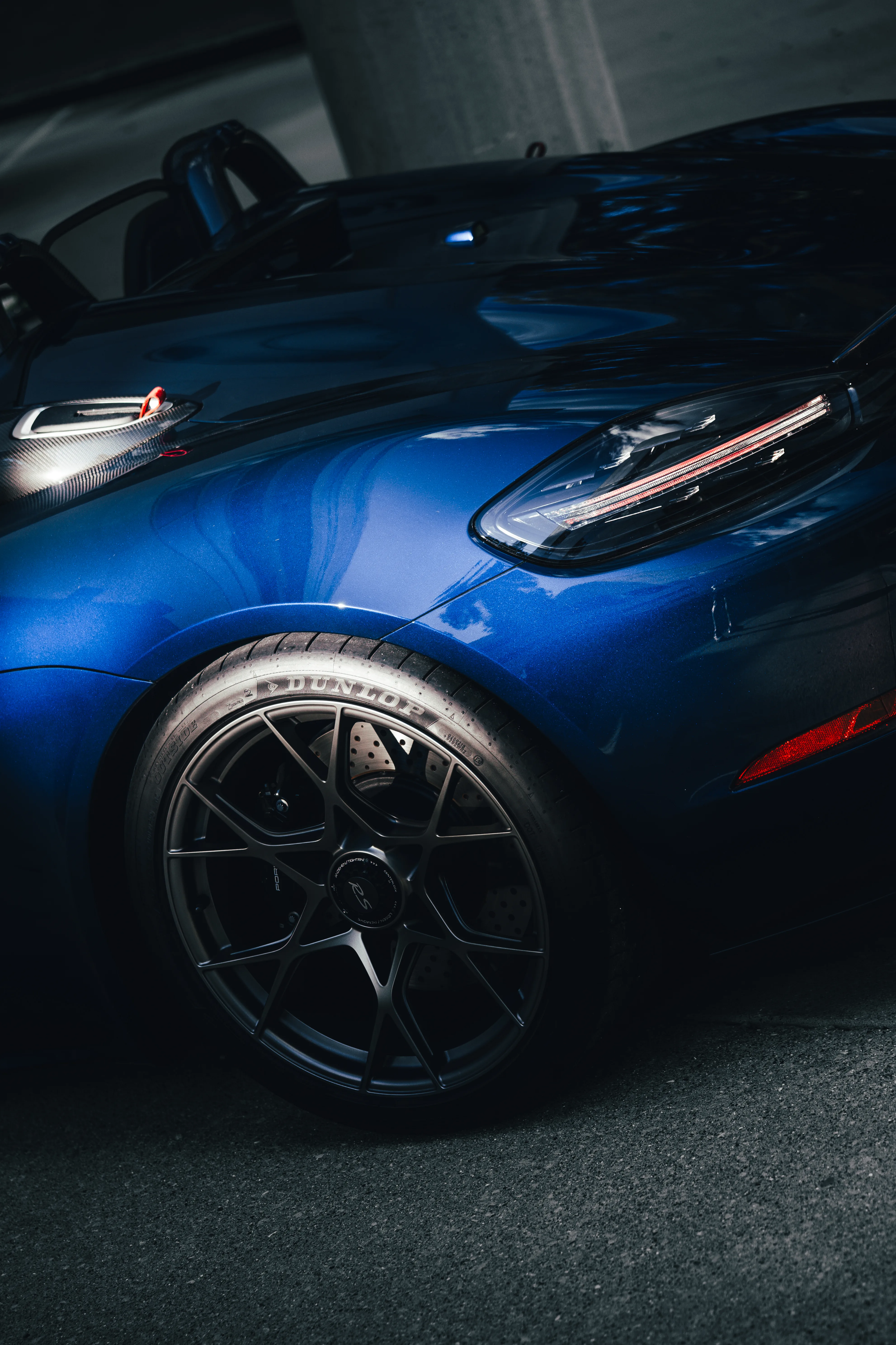 Close-up of a navy Porsche 718 Spyder RS's front fender, headlight, and wheel with a Dunlop tire.