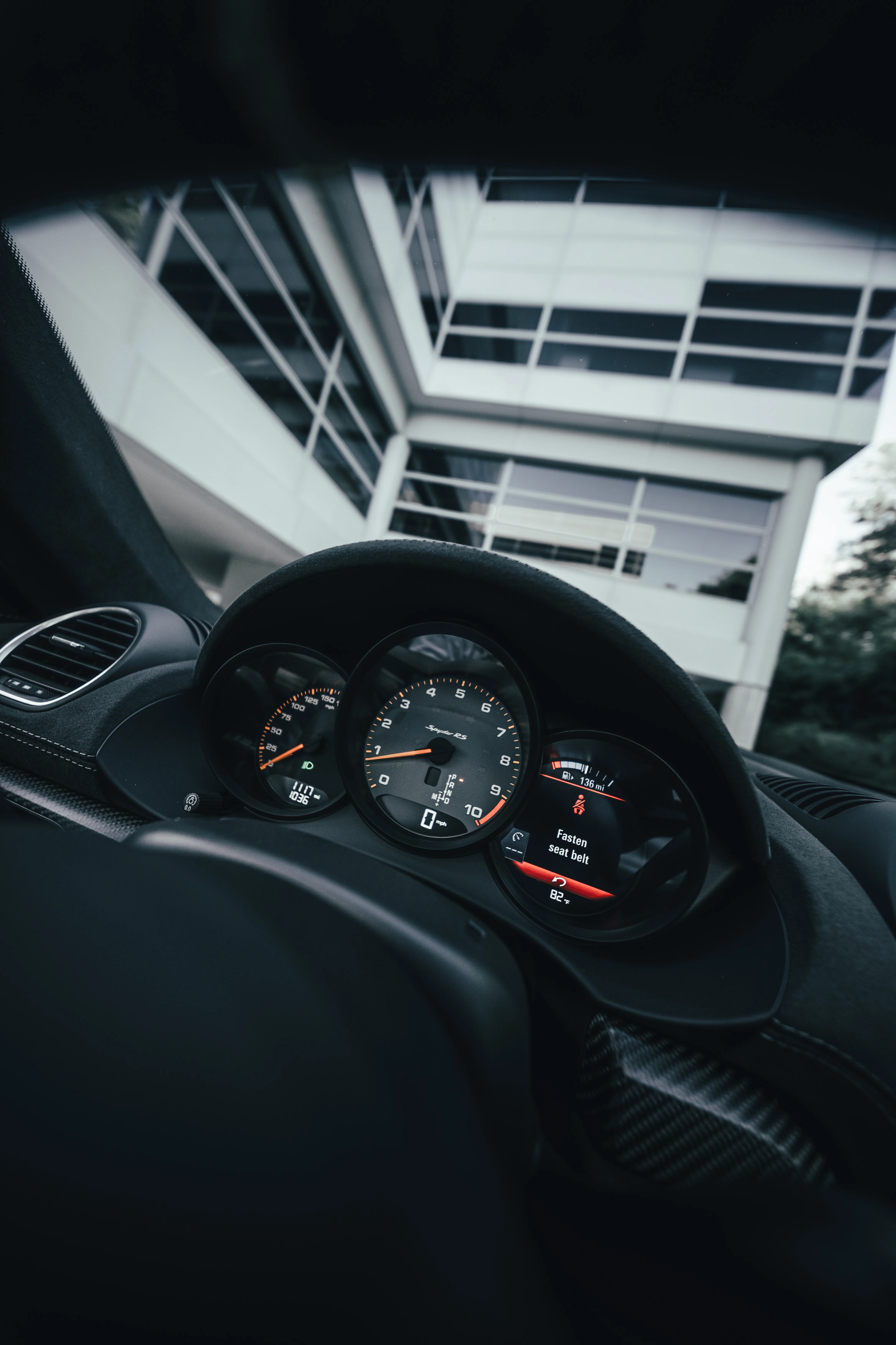 View from the driver's seat of a Porsche Spyder RS, showing the gauge cluster and a parking structure through the windshield.