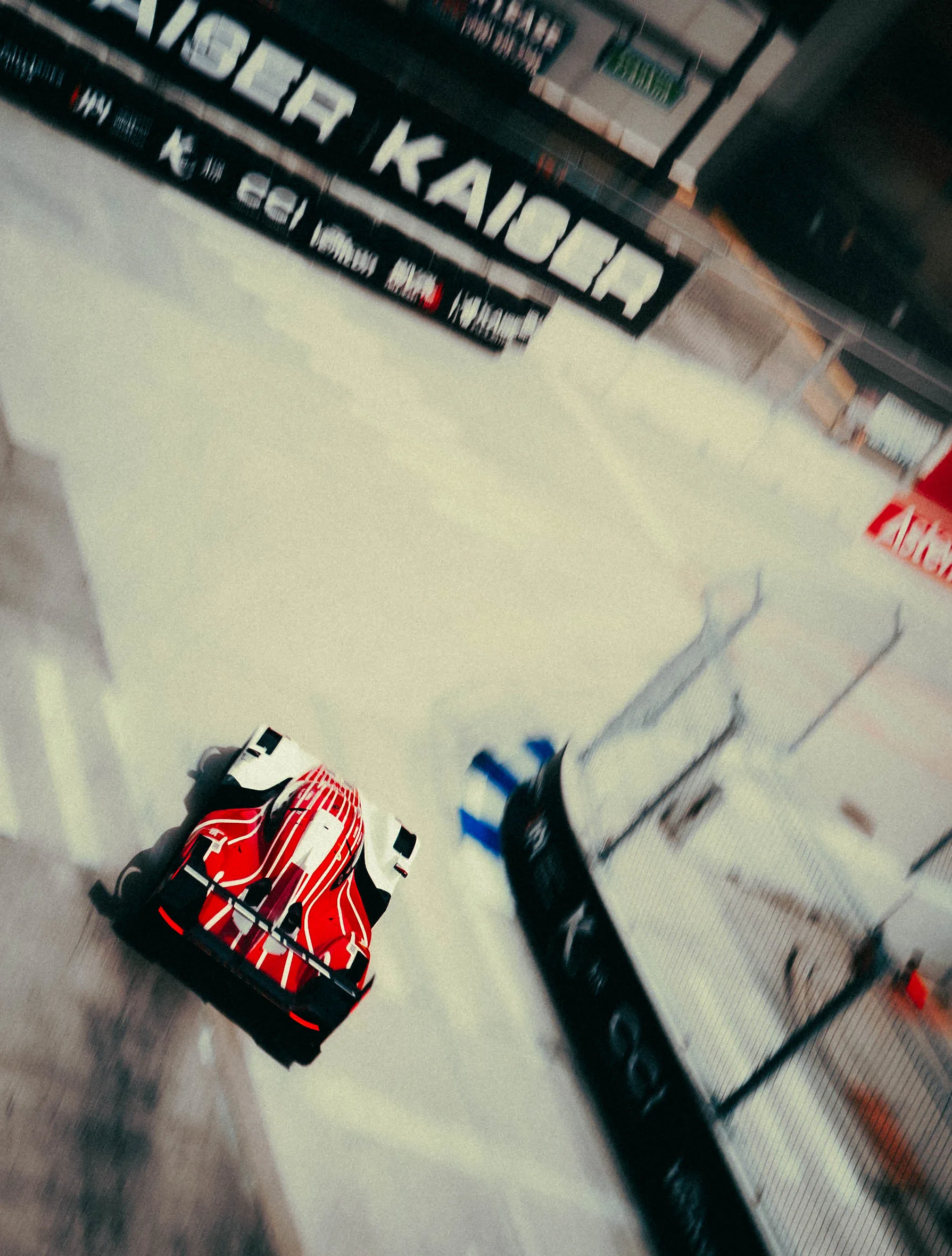 Overhead panned shot of a red and white prototype race car with 'KAISER' branding cornering on a street circuit.
