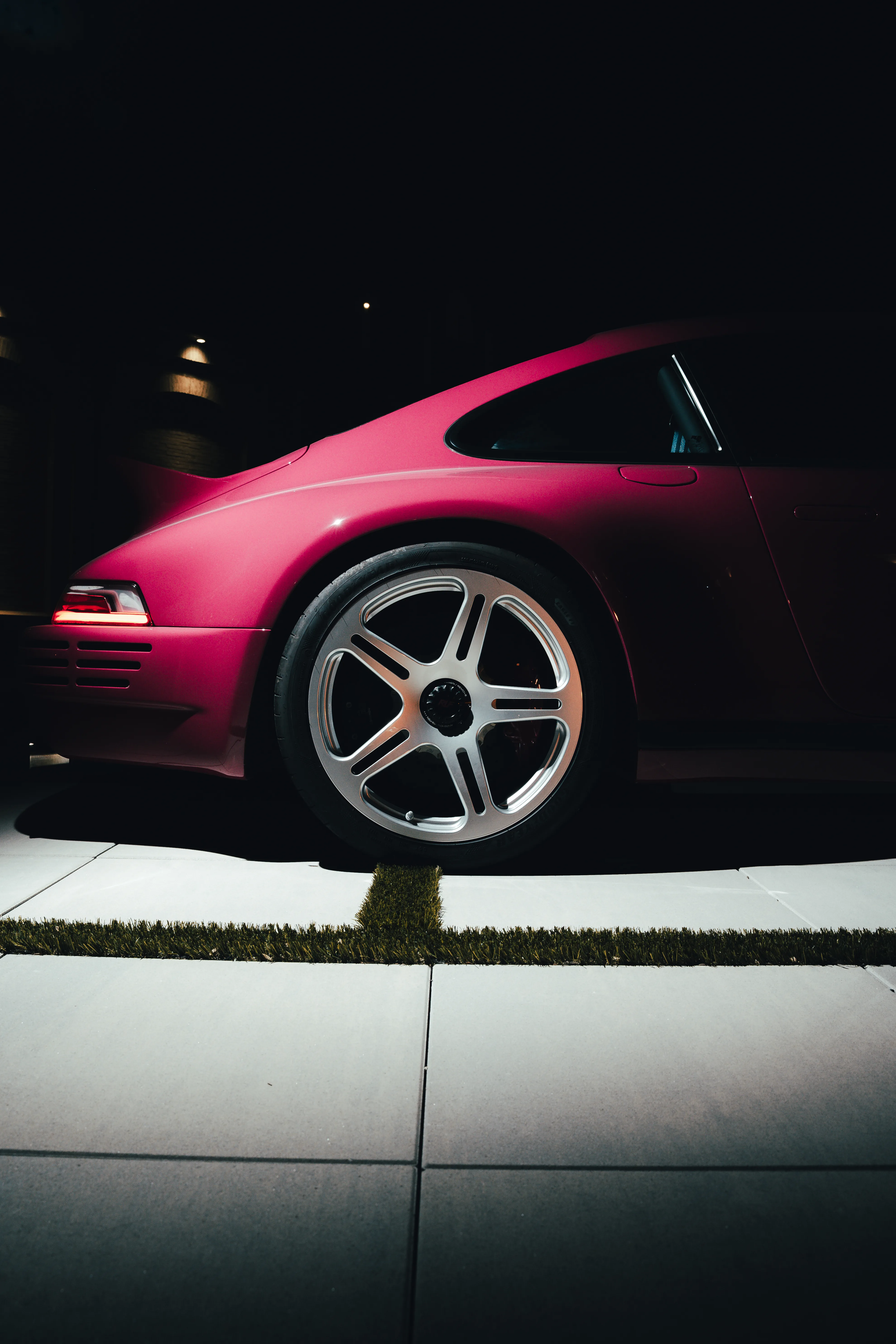Side profile of a magenta Porsche's front wheel and fender, lit dramatically against a dark background.