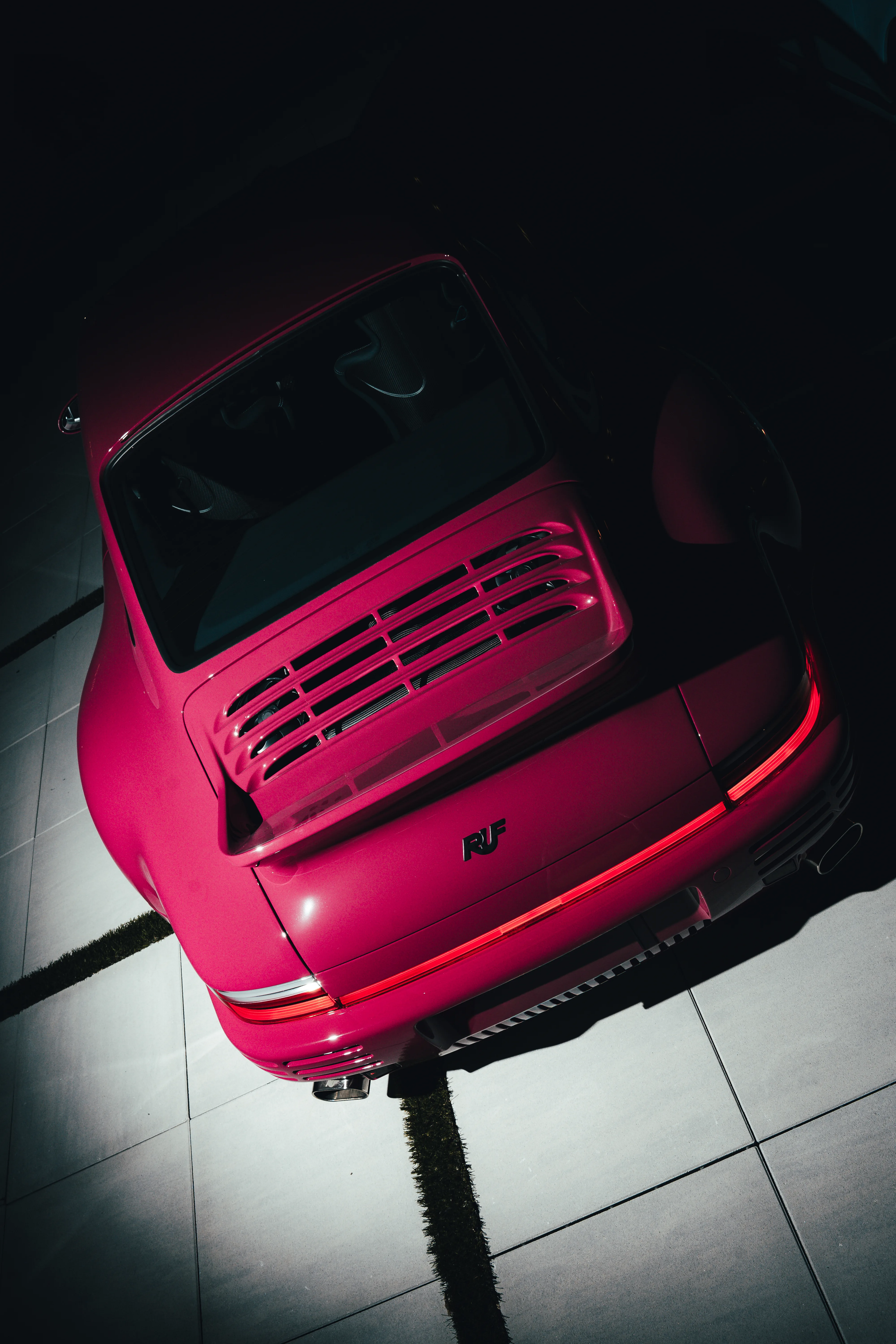 Overhead view of a light blue RUF's rear deck lid open, revealing its engine bay, taillight glowing red.